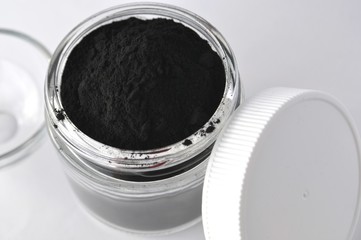 Activated charcoal powder for cosmetic face mask in a jar top view with copy space