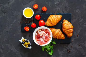 fresh croissants, bacon, tomatoes on a black background. top view. idea for breakfast