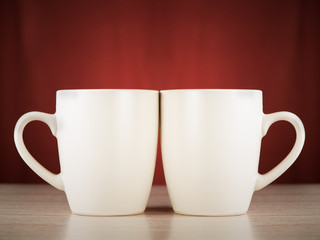 Two cups on a wooden surface on a dark red background