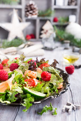 Fresh salad with smoked salmon, shrimps, raspberries and cherry tomatoes on white wooden background. Delicious Christmas themed dinner table