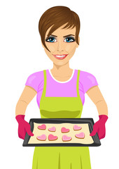 young woman holding baking tray with heart shape cookies