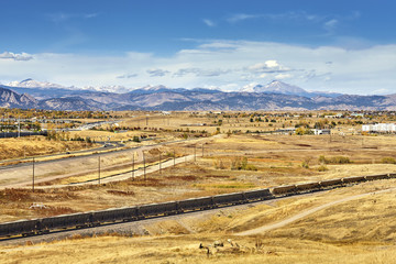 Autumn rural landscape with cargo train and Rocky Mountains in distance, Colorado, USA.