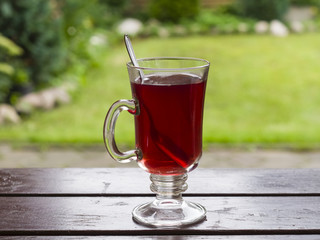 Red fruit tea in glass cup with spoon on wooden table, bokeh background, selective focus, shallow DOF