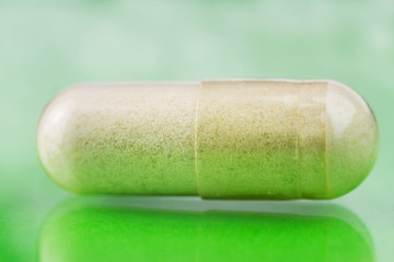 Glucosamine capsule, food supplement pills on glossy green background, macro image.