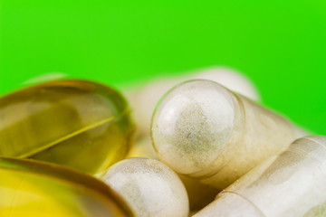 Mixed natural food supplement pills, omega 3 and glucosamine capsules on green background.