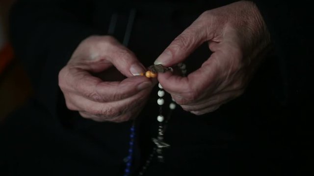 closeup of old woman’s hands praying and holding a rosary
