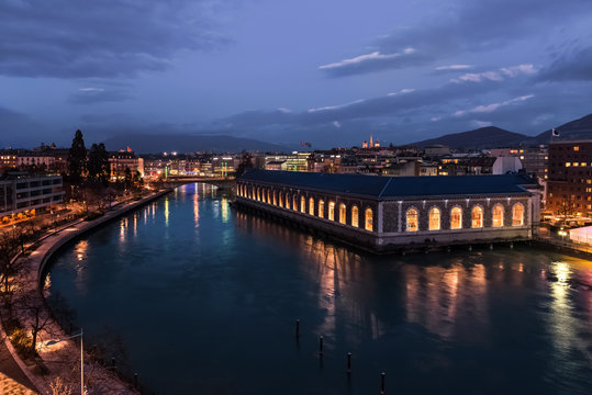 Famous building Batiment Forces-Motrices in Geneva at night. Landmark with view on the Rhone river and Saint-Piere cathedral.