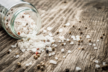 Whole peppercorns and crystal sea salt spilling from jar