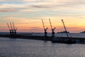 une digue et ses grues devant sur le port de Marseille, au coucher de soleil, depuis les terrasses du port