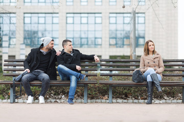 Two young friends curiously watchinga a young lady on the other bench.