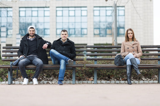 Group of young people is sitting on park benche on the street.