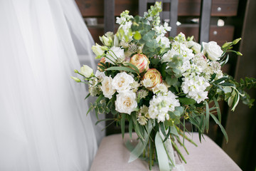 Bridal bouquet. The bride's . Beautiful  of white flowers and greenery, decorated with silk ribbon, lies on vintage wooden chair