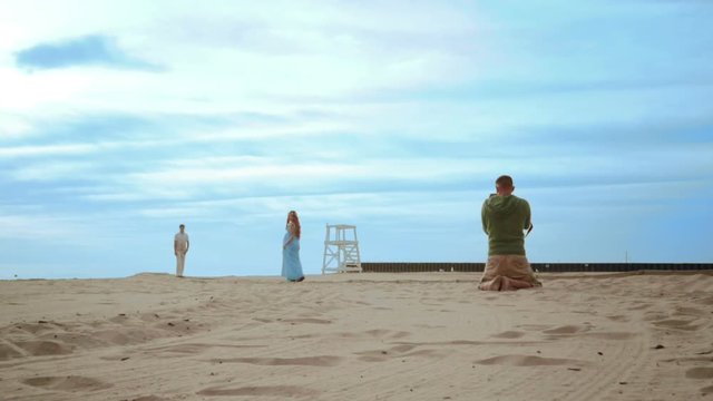 Romantic photo session on sea beach. Professional photographer beach. Man taking picture of pregnant couple on beach. Photographer sitting on beach. Photo shoot of love couple on beach