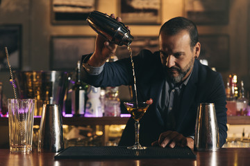 Barman is making cocktail at night club.