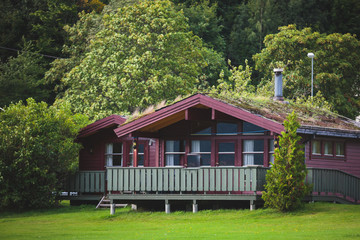 Beautiful landscape with classical scandinavian camping cottage wooden house cabin chalet hut, on a lake fjord shore coastline, in sunny summer day in Norway
