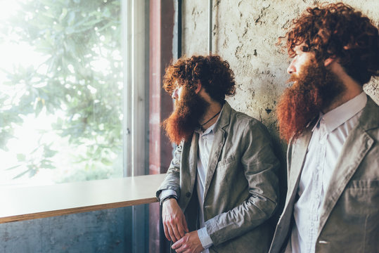 Identical male hipster twins looking out of office window