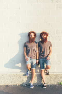 Bearded male twins standing by wall