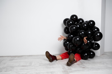 Girl sitting in black baloons stretching hands over white wall.