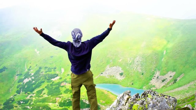 Beautiful mountain landscape with lake in Carpathian mountains. Young man standing on the top with raised hands. Slow motion 4K footage