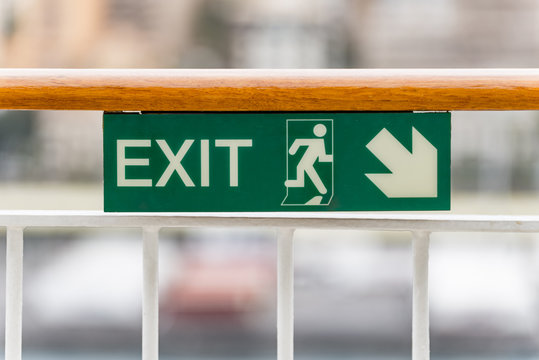 Attention green Exit sign with arrow on wooden railing cruise ship