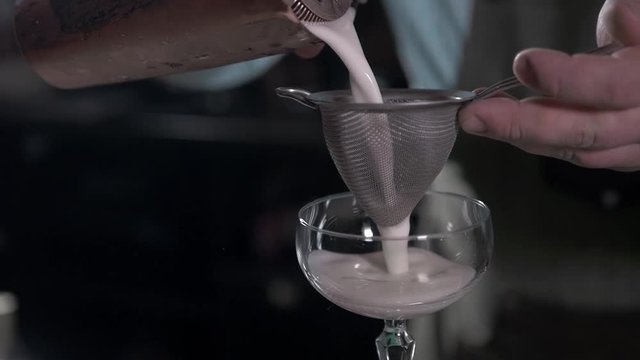 Bartender preparing coctail pouring through sieve close up in bar