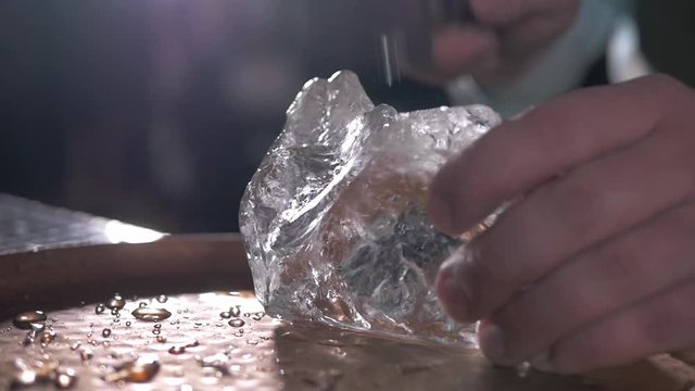Bartender chopping big ideal ice cubes by khife. Barmen ice figure.