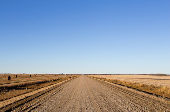 Gravel road dividing harvested fields and round straw bales in rural countryside autumn landscape