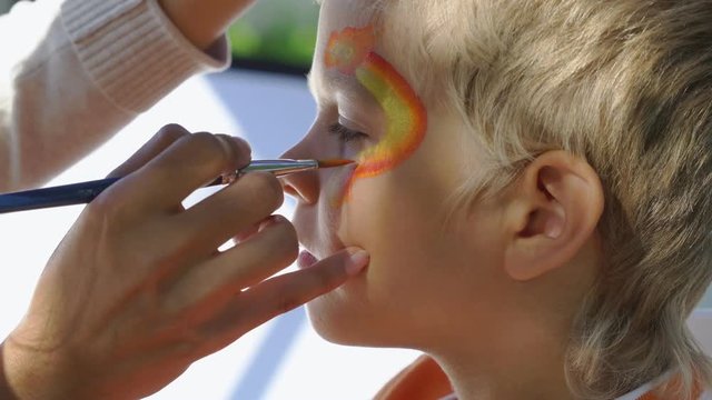 Professional artist paints with a brush on the face of a child a wavy line. Animator draws akvagrim drawing on the boy's face close up.