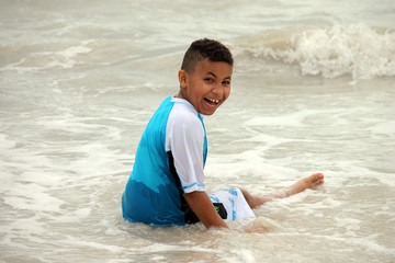 Young Biracial Boy Sitting in the Ocean and Smiling