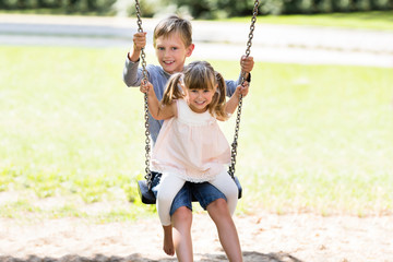 Brother and Sister Enjoying On Swing In The Park