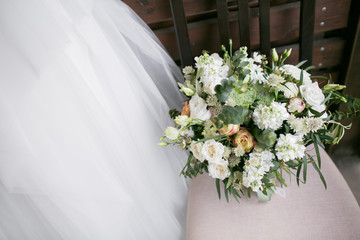 Bridal bouquet. The bride's . Beautiful of white flowers and greenery, decorated with silk ribbon, lies on vintage wooden chair