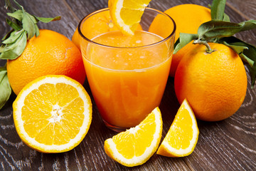 glass of fresh orange juice and oranges on wooden background