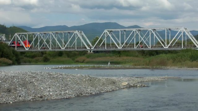 Электричка проходит по железнодорожному мосту через реку 