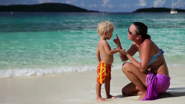 mother putting sunscreen on child at tropical beach in the Caribbean