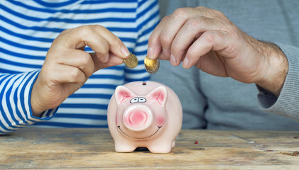 Sparen, Anlegen, Rente - zwei Seniorenhände werfen Geld ins Sparschwein