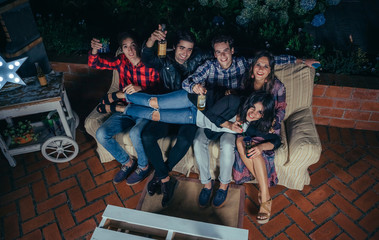 Happy young woman lying over group of friends on sofa in a outdoors party. Friendship and celebrations concept.