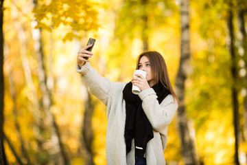 Young girl take selfie on phone with cup of coffee on yellow sunny park