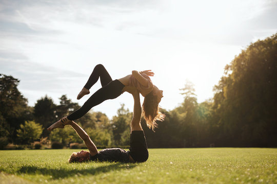 Fit couple doing acrobatic yoga exercise in park