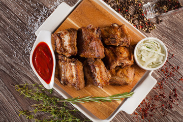 pork ribs grilled on a wooden board with a white plate, scattere