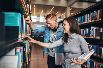 Two young students at library book shelf
