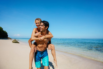 Happy young couple piggyback on tropical beach
