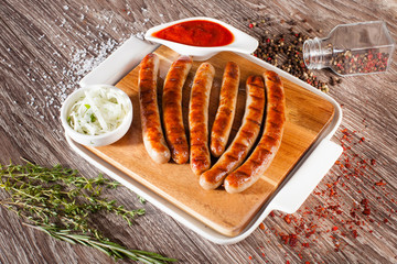 Sausages grilled on a wooden board with a white plate, spices an