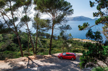 Seascape of Mediterranean Sea with a red car  traveling on the mountain serpentine through the pine forest along the coast of Mallorca. Auto travel and roadtrip concept - 127383354