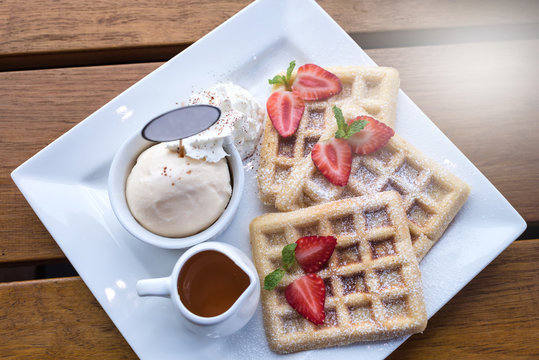 Strawberry waffle and honey with ice cream on wooden table, selective focus, lights effects.