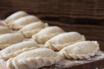 Prepared for cooking vareniki, dumplings, pierogi on a floured wooden board - traditional Ukrainian food. Selective focus