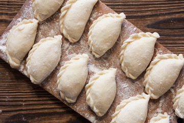 Prepared for cooking vareniki, dumplings, pierogi on a floured wooden board - traditional Ukrainian food. Selective focus