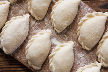 Prepared for cooking vareniki, dumplings, pierogi on a floured wooden board - traditional Ukrainian food. Selective focus