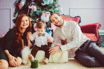 Happy parents and their cute little son sitting near Chistmas tr