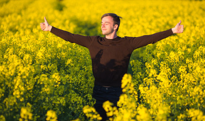 man in yellow canola field blowing his nose and suffering from pollen allergy.