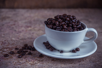 Spilled coffee beans from the white ceramic cup on the wooden ba